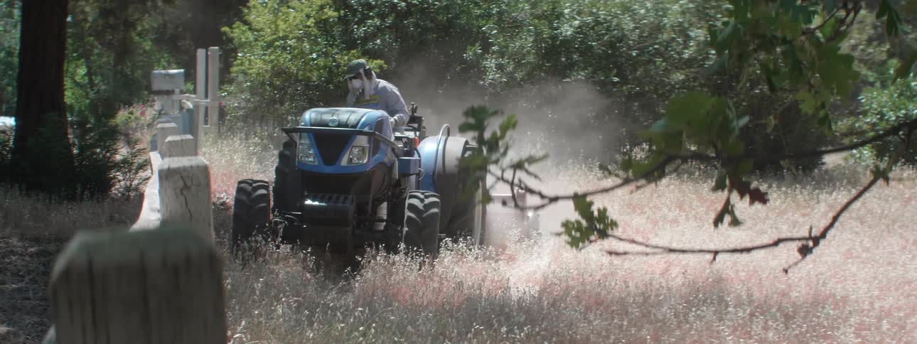 A farmer driving through weeds in a field on a tractor
