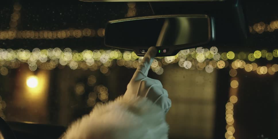A person with gloves touching a button on a rearview mirror in a vehicle