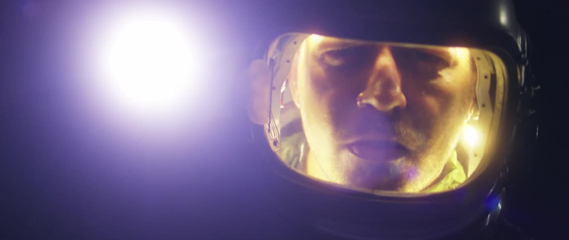 A man wearing a helmet holds and shines a bright flashlight