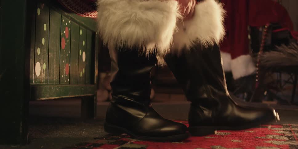 A man dressed as santa claus sits on a wooden bench while putting on his boots
