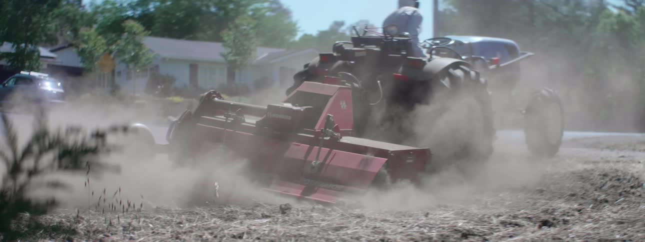A person drives a tractor that is pulling a large plow behind it