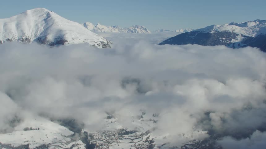 Clouds hover over a snowy mountain valley on a sunny day