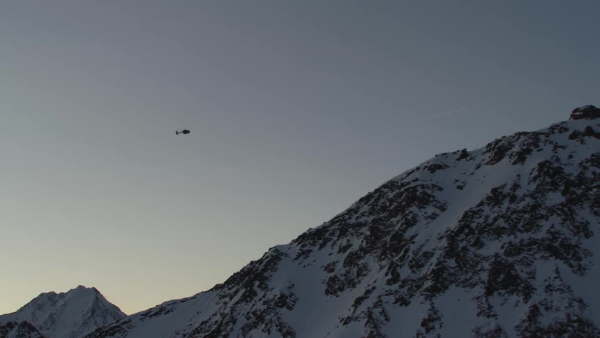 A helicopter flies high about snowy mountaintops