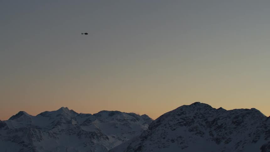 A helicopter passes over a vast mountain range