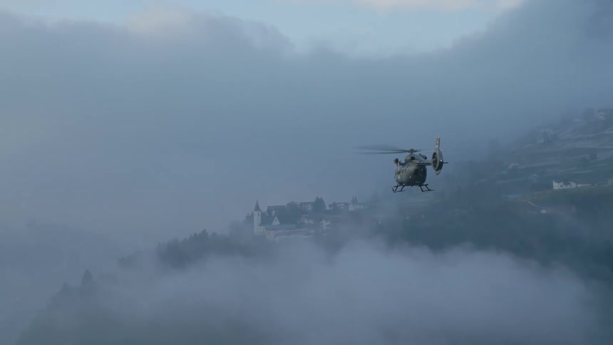 A helicopter flying in the air with buildings trees the sky and clouds in the background