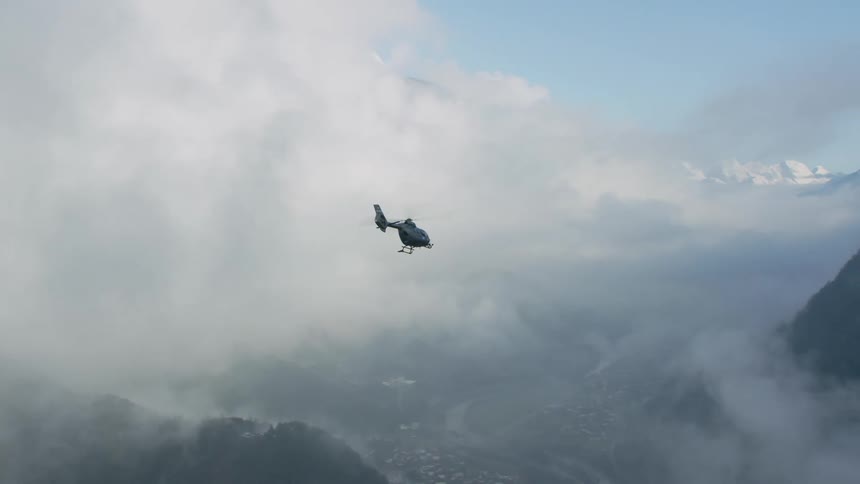 A helicopter flies through clouds over mountain valley