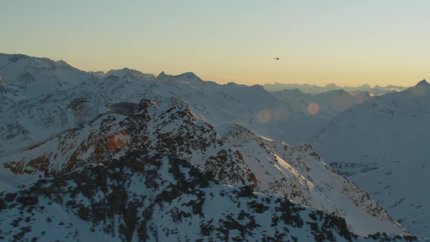 A helicopter flying over a snow covered mountain range with the sky and clouds in the background