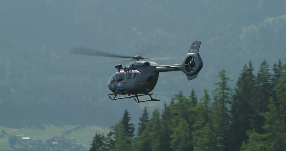 A helicopter flies above mountain forest trees and valley