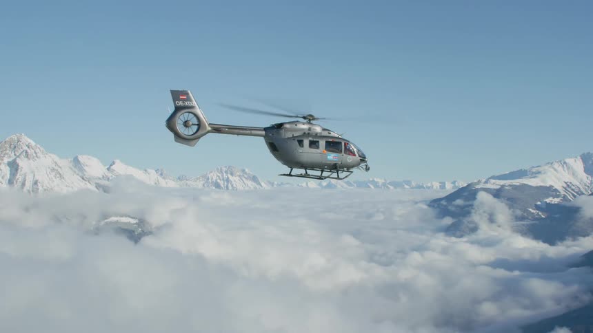 Helicopter flies over the snowy mountains under a blue sky