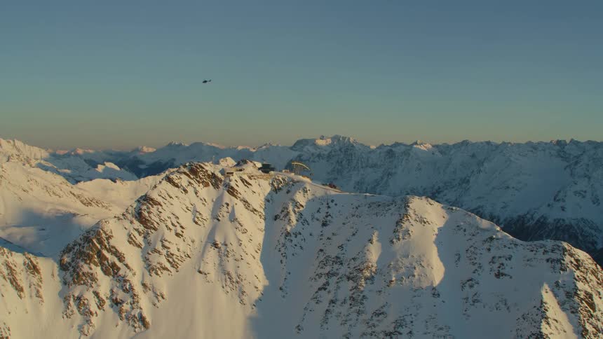 A helicopter flying over a snow covered mountain range with the sky and clouds in the background