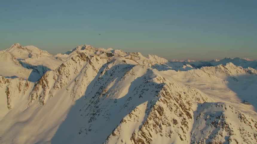 A helicopter flying over a snow covered mountain range with the sky and clouds in the background