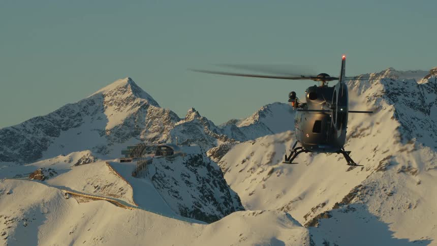 A helicopter flies over snow capped mountains