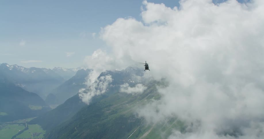 A helicopter flying over a large mountain range on a cloudy day