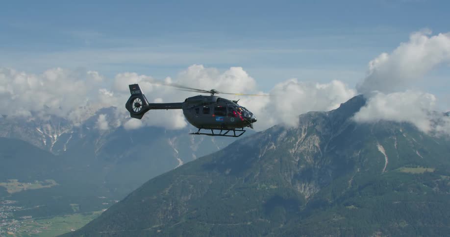 Helicopter flies over mountains as mist covers town occupying valley amid mountain range