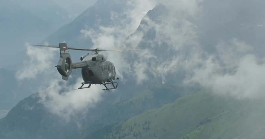 A helicopter flies through fog and clouds heading toward mountains