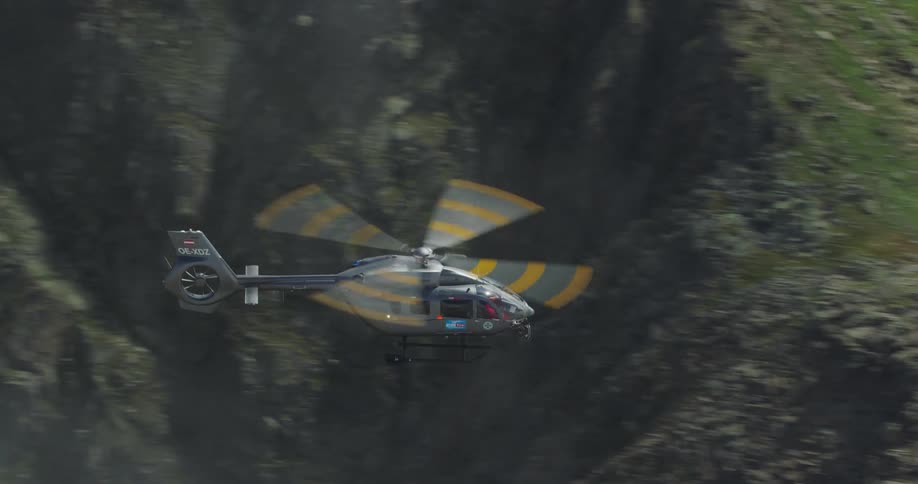 A helicopter flies above green rocky ridges then cloud cover