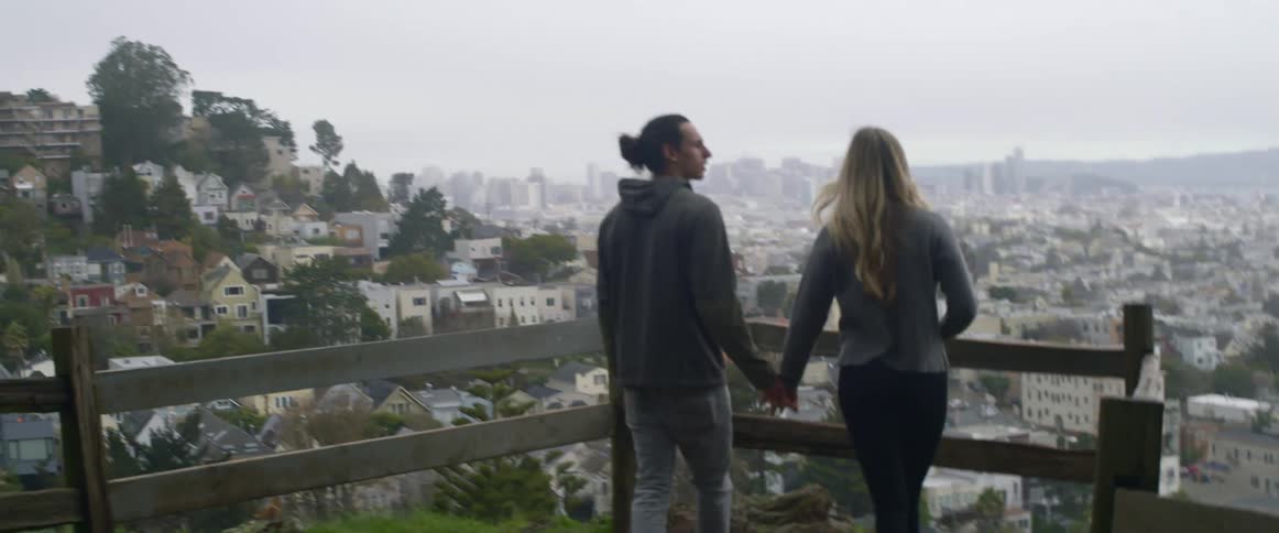 A man and women walk to a railing above a town