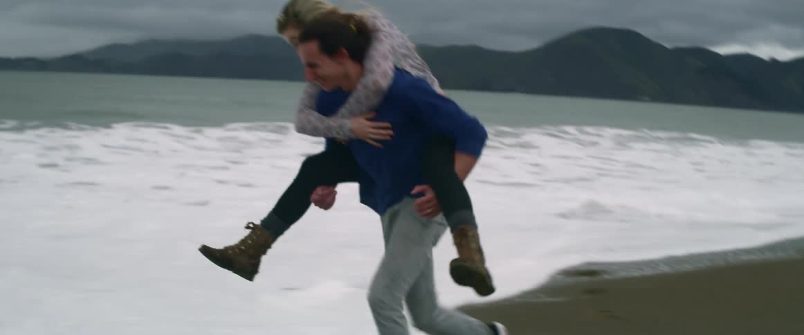 Man running on a beach while his girlfriend is piggybacking