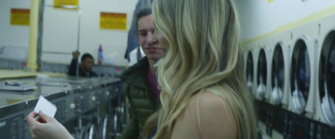 A couple chats, smiles and looks at a freshly taken photograph in a laundromat