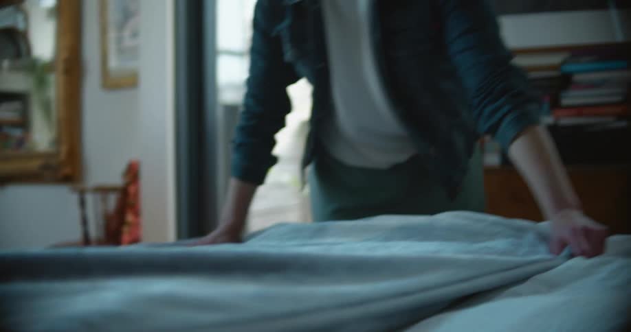 A woman makes a bed indoors during the day