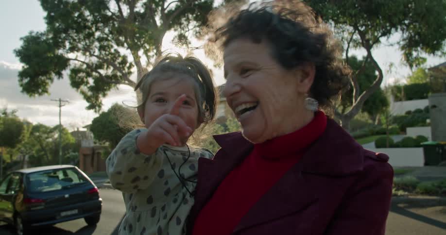 A woman smiles while holding her granddaughter as they stand in front of their house