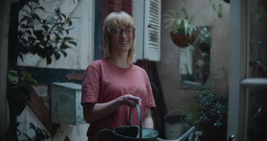 A woman is holding a water can as she stands in a room full of plants