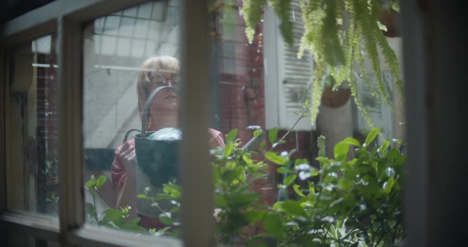 A woman uses a watering can to water plants in her yard
