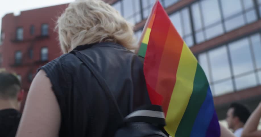A person carries a rainbow flag while participating with others in a city pride march