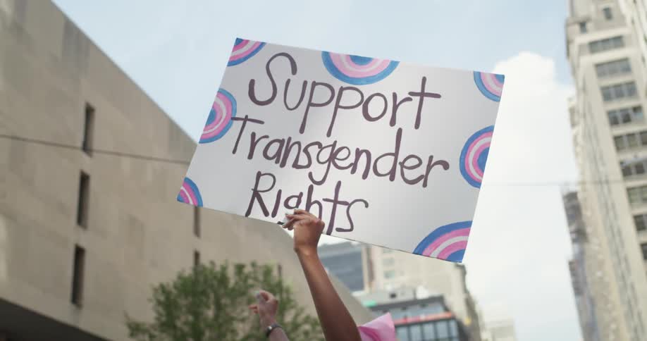 Person holds sign for transgender rights at rally downtown under cloudy sky