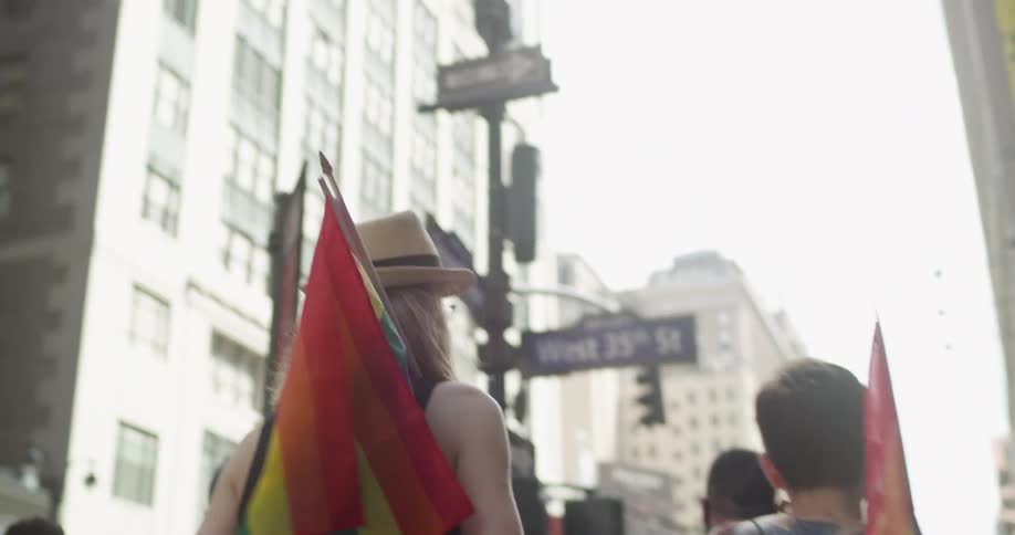 A man and woman holding gay pride flags march down a city street alongside a crowd