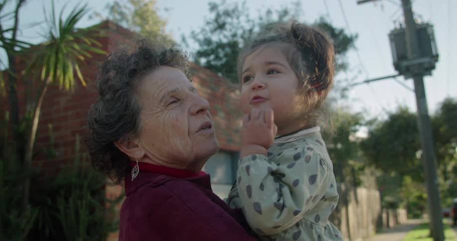 A grandmother holds her granddaughter as the little girl points to something in the distance that excites them