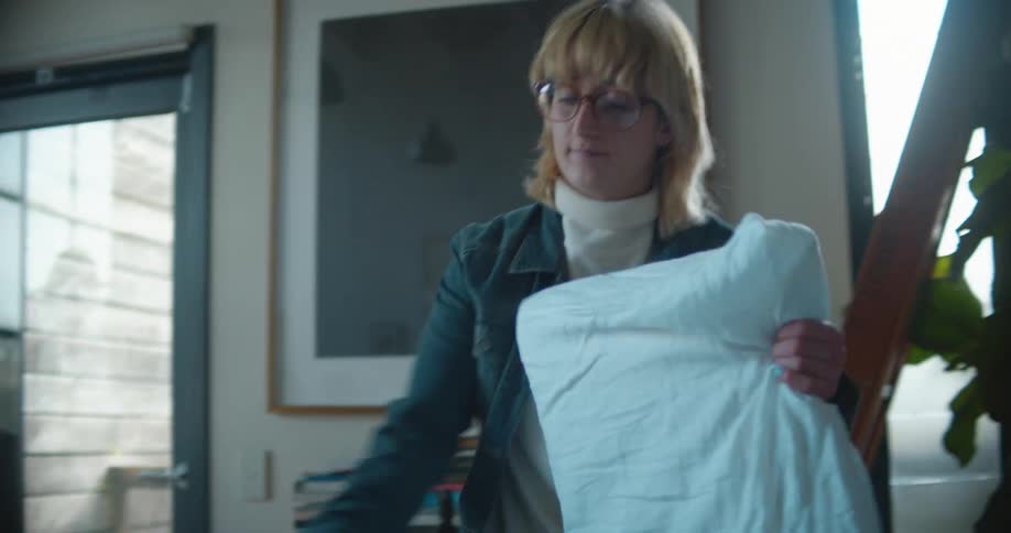 A woman is walking in her house and holding pillows