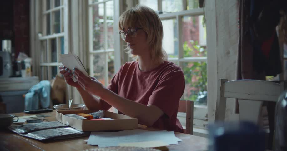 A woman looking through photographs while sitting at a home dining table