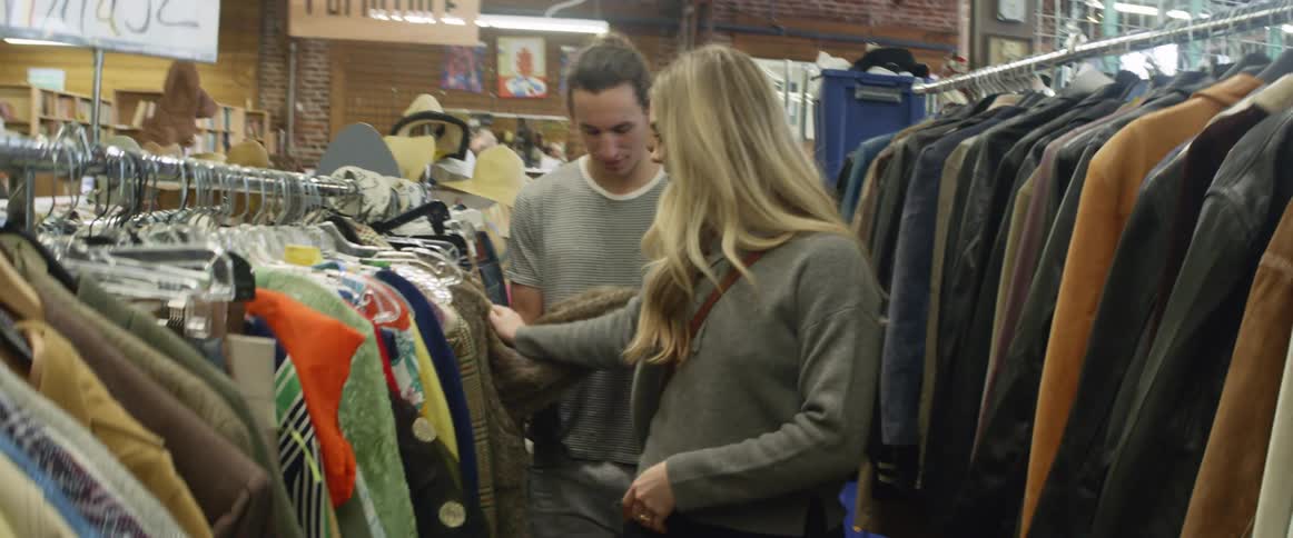 Two people are looking through clothes in a store