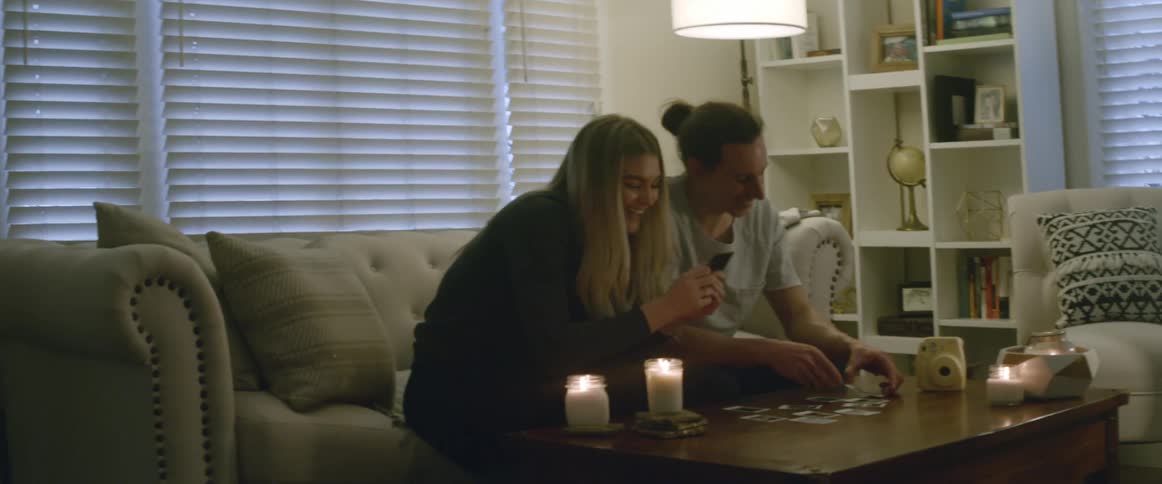 Two people sit on a couch together examining items on a table