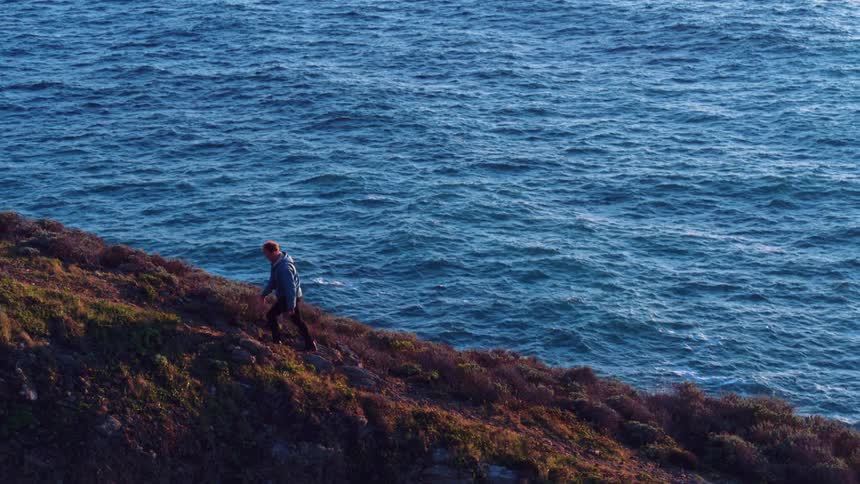 A man climbs up a steep ocean side hill
