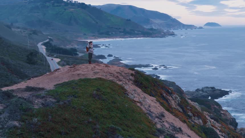 Blonde woman stands on the top of mountain just to see the landscape of the seashore on a cloudy day