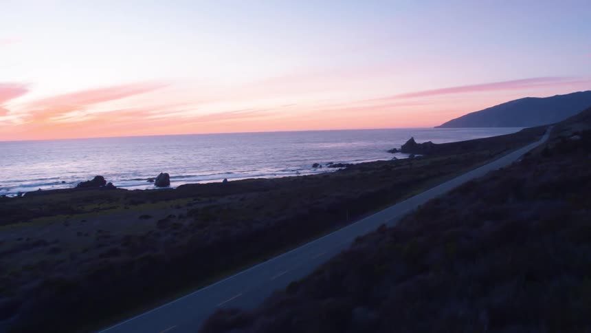A car speeding down a road near a coast at sunset