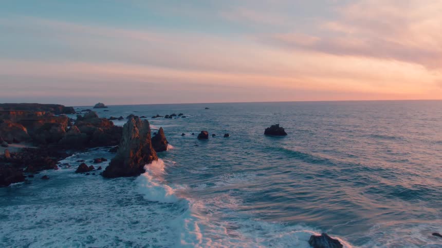 An aerial view of the ocean and a rocky coastline at dawn