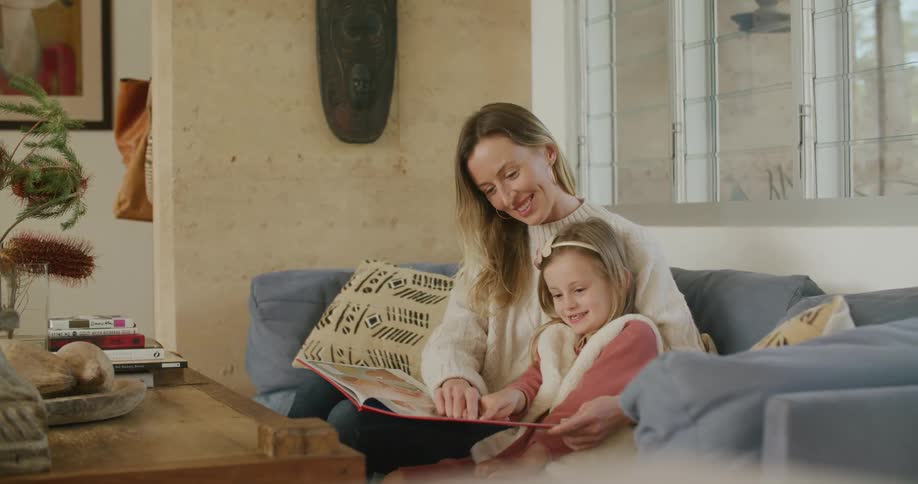A woman and a girl in a room sitting on a couch reading a book