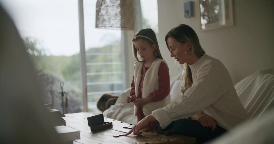 A woman shows her daughter who to play a game in the living room of a house during the day