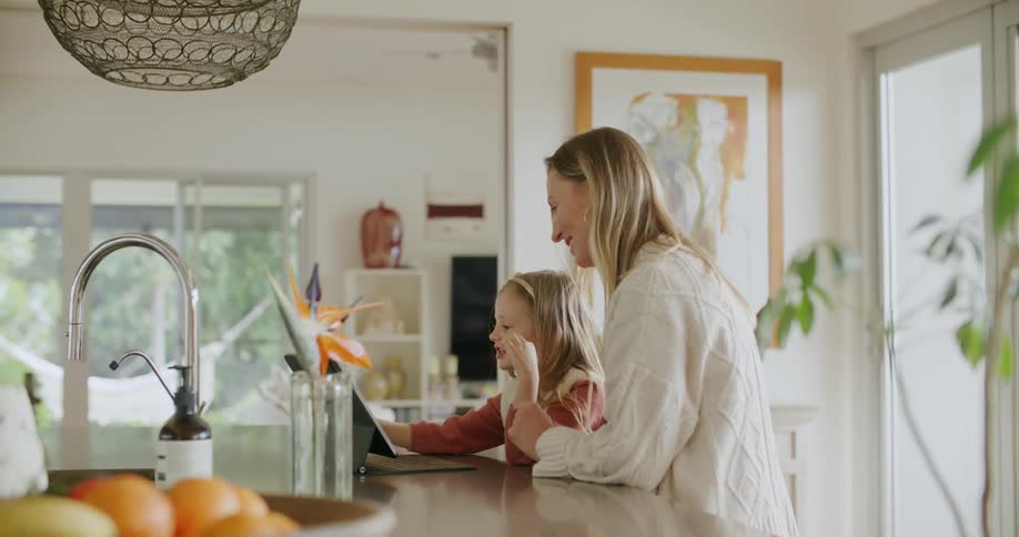 Mother and daughter sit at kitchen island making selections on tablet