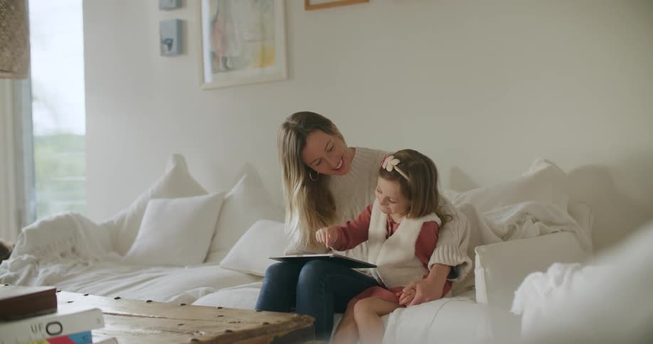 Mother and daughter sitting in a couch at home using a tablet