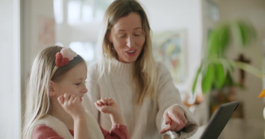 Mother and daughter sit smiling and talking as they interact with tablet with keyboard attached