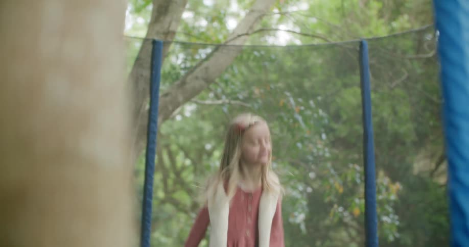 Mother watches daughter bouncing on trampoline strewn with fallen leaves