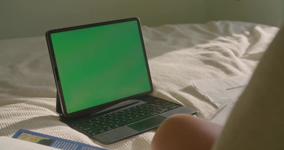 Woman working on bed in front of a laptop with a green replaceable screen
