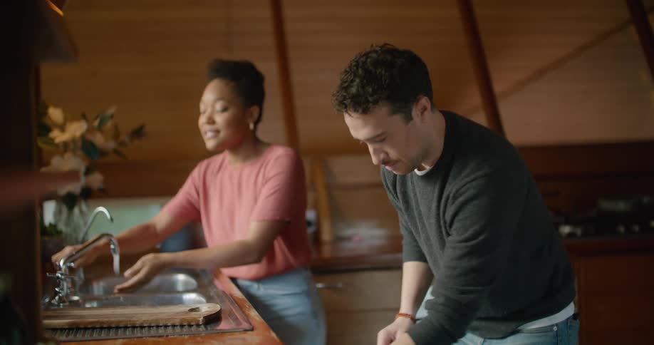 A woman washes a butter knife and hands it to a man to place in the dishwasher
