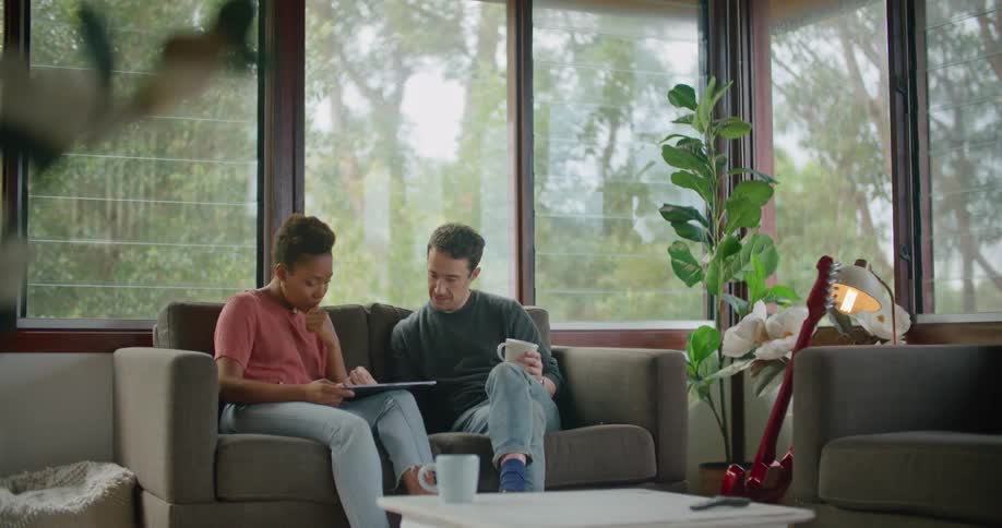 A couple scroll through a tablet together while sitting on the couch