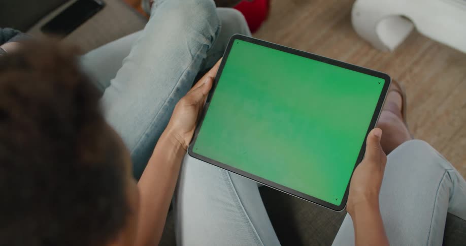 Man and woman wearing jeans sit on couch and use tablet with green screen