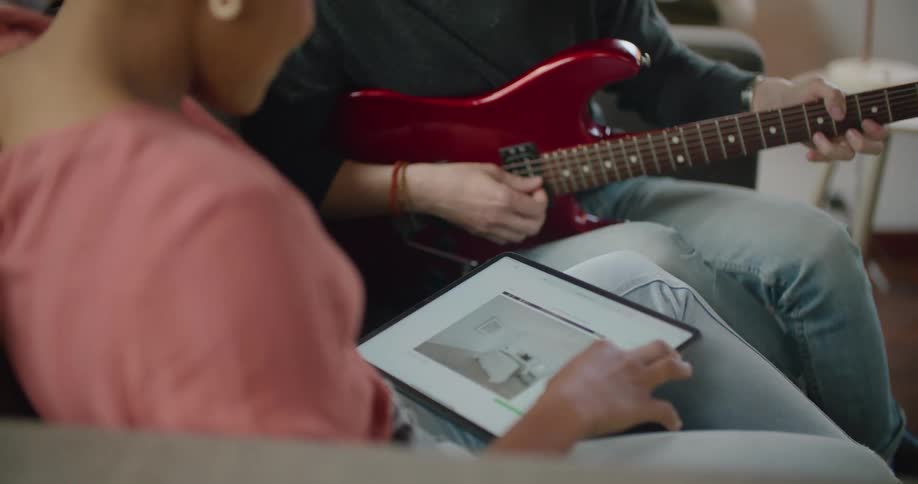 A man stops playing guitar to look at interior design ideas on a tablet with his girlfriend as they sit at home